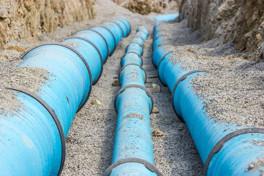 Three blue HDPE watermain pipes laid side by side in an open trench of sand and gravel