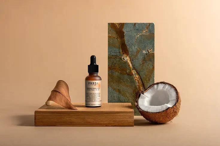 Freja facial toner bottle styled on a wooden block with a halved coconut and a slab of stone