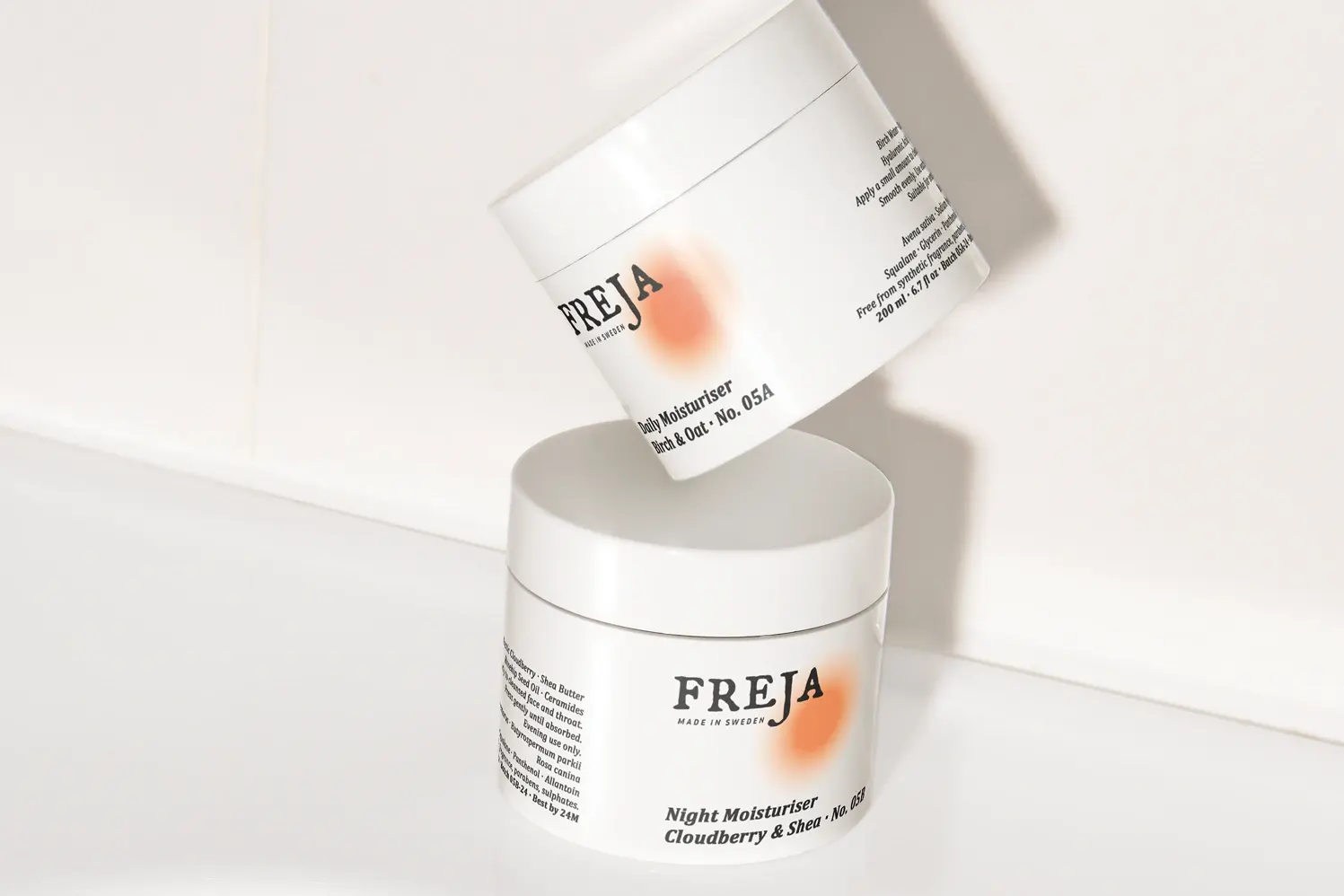 Two Freja moisturizer jars stacked on a white tiled surface