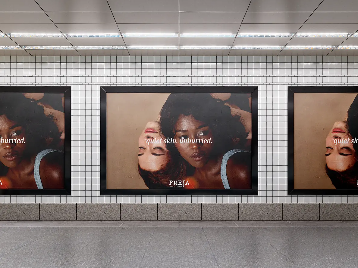 Subway platform billboard ad for Freja showing two models with eyes closed, reading quiet skin. unhurried.