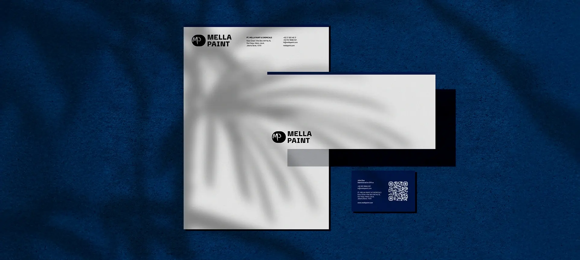 Mella Paint stationery mockup: navy envelope and business card on a dark fabric background
