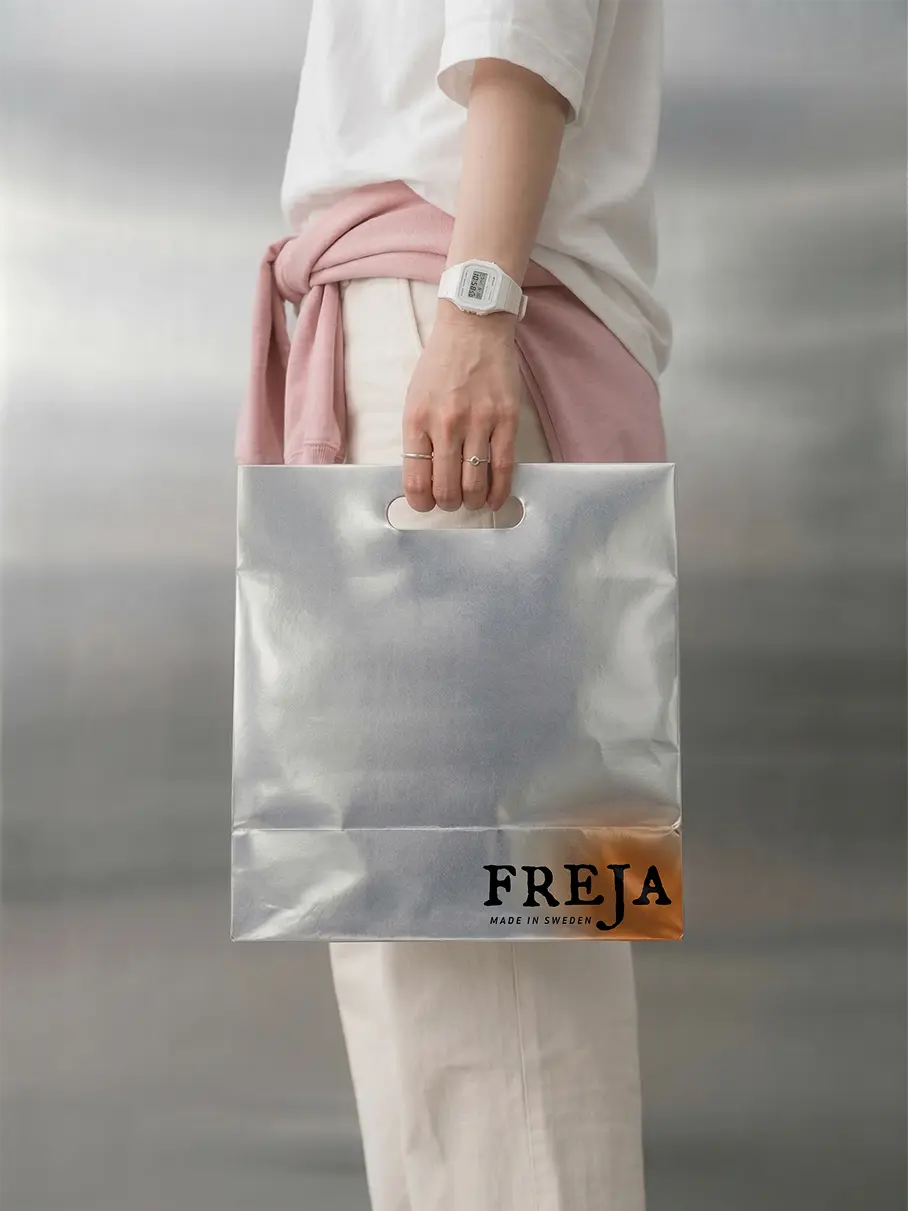 A model carrying a metallic silver Freja shopping bag with the wordmark printed in black